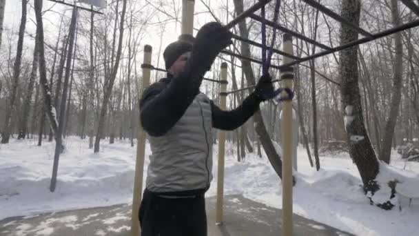 Fitness man using expander for outdoor training on sports ground in winter park. — Stock Video