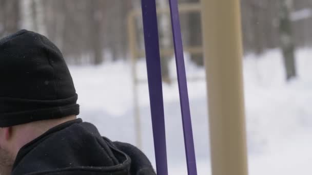 Hombre que utiliza expansor de fitness para hacer ejercicio en cuclillas en el entrenamiento de invierno en el campo deportivo — Vídeos de Stock