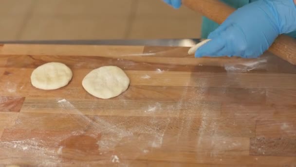Пекарь в перчатках катит тесто для выпечки на деревянном столе в пекарне — стоковое видео