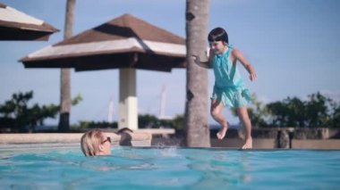 A single mom enjoying a vacation swimming in the pool with her little daughter.