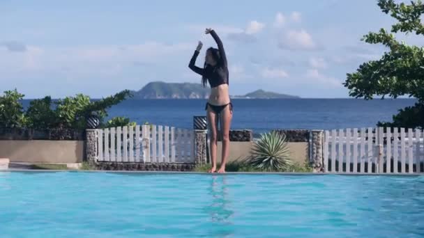 Ασιάτισσα κάνει ασκήσεις τεντώματος, καταδύσεις στην πισίνα στο φόντο λόφους της θάλασσας. — Αρχείο Βίντεο