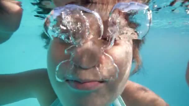 Kind meisje speelt onder water, kijken naar de camera en het maken van bubbels. — Stockvideo