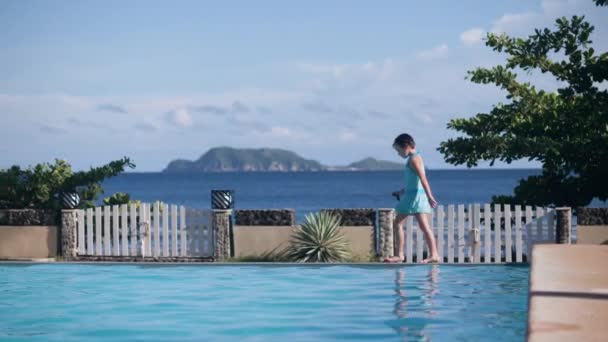 Niña está caminando cerca de la piscina en el hotel tropical en el fondo del mar y las colinas . — Vídeo de stock