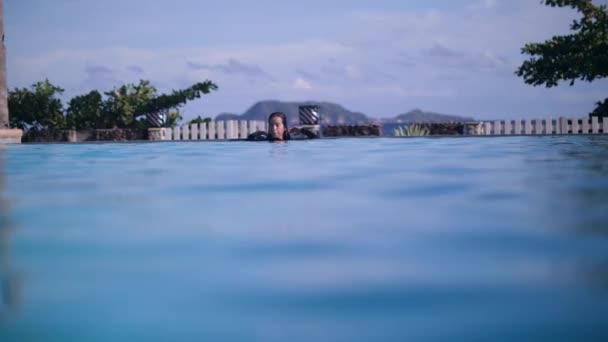 Aziatisch meisje baden in zwembad met een geweldig natuurlijk uitzicht op de oceaan en de bergen. — Stockvideo