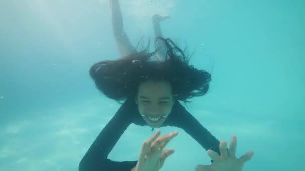 Feliz chica asiática mirando a la cámara, sonriendo bajo el agua y agitando las manos en la piscina . — Vídeo de stock