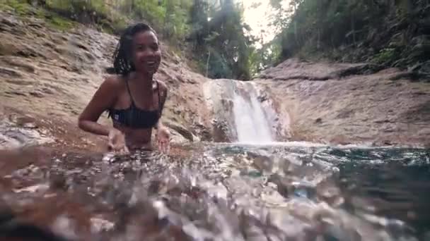 Una joven feliz se sienta en un arroyo de agua cerca de una cascada . — Vídeo de stock