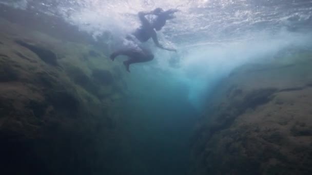 Unterwasseraufnahmen: Junge Touristin springt in Zeitlupe in Wasserfall. — Stockvideo