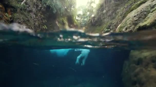 Eine junge Frau im Urlaub springt zu einem Wasserfall und schwimmt unter Wasser. — Stockvideo