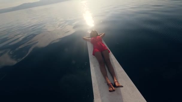 Жінка лежить на краю вітрильного човна, насолоджуючись схід сонця в морі . — стокове відео
