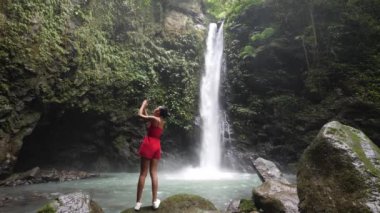 Şelalede duran genç bir turist akıllı telefon kullanarak fotoğraf çekiyor..