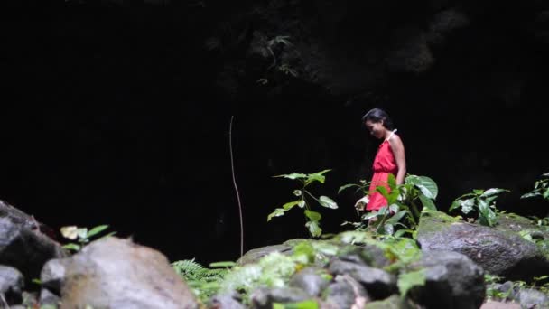 Mujer vestida de rojo caminando sola en un estrecho y húmedo barranco oscuro en la selva . — Vídeos de Stock