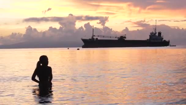 En glad ung flicka hoppar och stänk vatten stående på stranden vid soluppgången. — Stockvideo