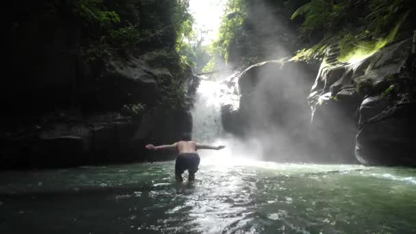 Caucasian guy jumps and swim in the tropical rainforest waterfall at summer day. — Stock Video