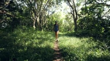 Genç bir kadın güneşli bir günde tropikal bir parkta yürüyor..