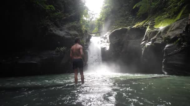 Männlicher Typ im Urlaub ist aufgeregt und hebt beide Hände im Wasserfall. — Stockvideo