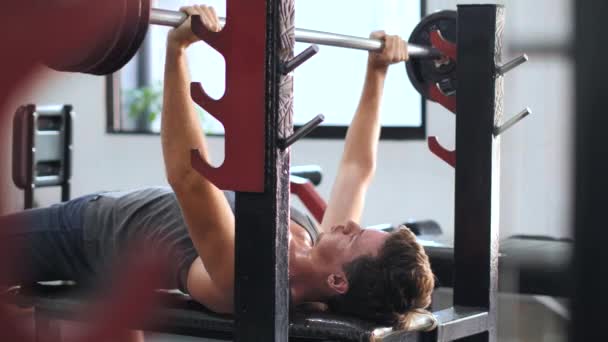 Ejercicio fuerte de la prensa del banco del entrenamiento del hombre joven en el gimnasio . — Vídeos de Stock