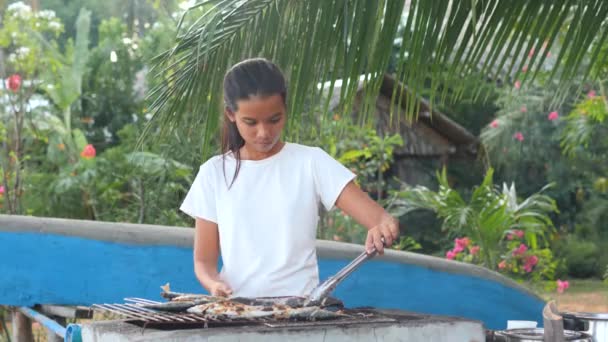 Молода азіатка готує смажену рибу на задньому дворі на тропічному тлі.. — стокове відео