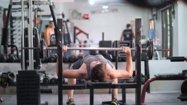 Un jeune homme faisant de l'exercice de presse sur banc dans la salle de gym . — Video
