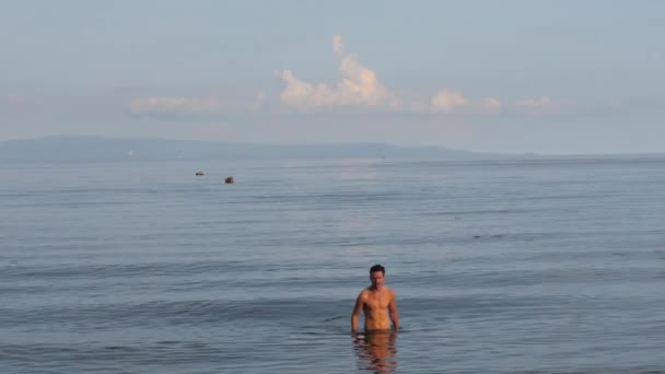 Ένας γυμνασμένος άντρας περπατά στην παραλία, στη θάλασσα. Καλοκαίρι και διακοπές έννοια. — Αρχείο Βίντεο