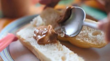 Çatal kullanarak beyaz ekmeğin üzerine fıstık ezmesi süren bir el. Yakın çekim.