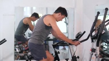 Spor salonunda bisiklet egzersizi yapan, bacaklarını çalıştıran, kardiyo antrenmanı yapan bir adam..