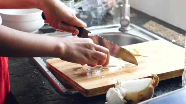 Close up shot of a womans hand slicing white onions on a wooden chopping board. — Stock Video