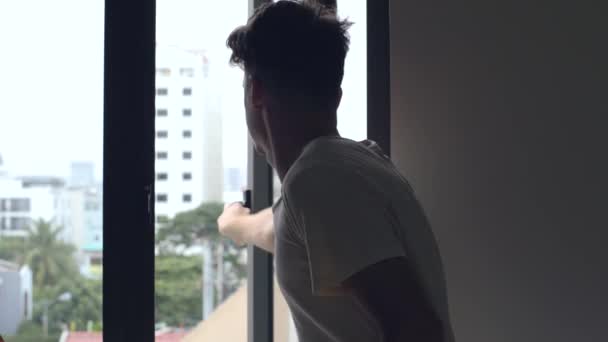 Um homem abre uma janela e fica olhando para a cidade com edifícios de vários andares . — Vídeo de Stock
