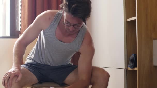 Молодой человек в очках сидит на стуле дома и делает упражнения . — стоковое видео