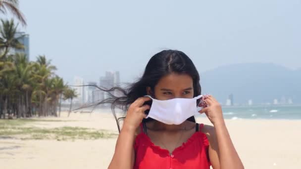 Asiatisk kvinna som står på stranden och bär ansiktsmask. Begreppet hälsa och säkerhet. — Stockvideo