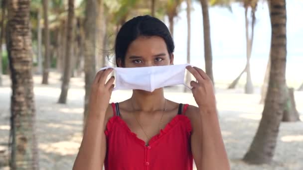 Giovane donna asiatica indossando maschera in spiaggia, palme bakground. — Video Stock