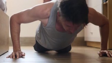 Kaslı genç adam evde yerde şınav çekiyor..