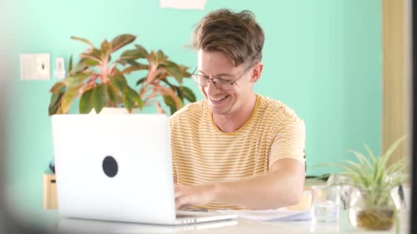 Un chico feliz riendo duro mientras estudia en casa delante de la laptop . — Vídeos de Stock