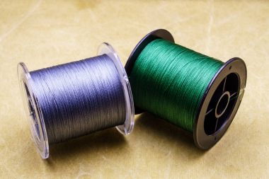 Spools of cords on the background of tarpaulin. Green and gray fishing line. Spools of braided fishing line clipart