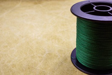 Spool of cord on the background of tarpaulin. Green fishing line. Spool of braided fishing line clipart