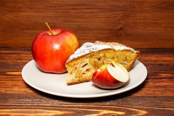 Manzanas frescas y un trozo de tarta de manzana espolvoreada con azúcar en polvo en el fondo de una tabla oscura . — Foto de Stock