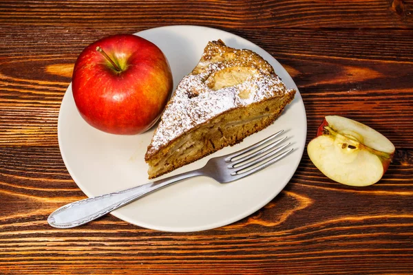 Manzanas frescas y un trozo de tarta de manzana espolvoreada con azúcar en polvo en el fondo de una tabla oscura . — Foto de Stock