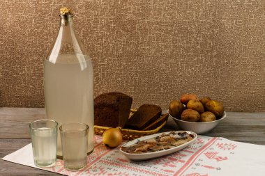 Ukrayna ulusal içecek ve atıştırmalık. Eski tahta masadaki büyük şişe ve bir bardak kaçak içki. Rus votka ve aperatif.