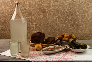 Ukrayna ulusal içecek ve atıştırmalık. Eski tahta masadaki büyük şişe ve bir bardak kaçak içki. Rus votka ve aperatif.