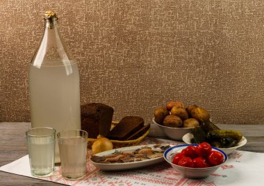 Ukrayna ulusal içecek ve atıştırmalık. Eski tahta masadaki büyük şişe ve bir bardak kaçak içki. Rus votka ve aperatif.