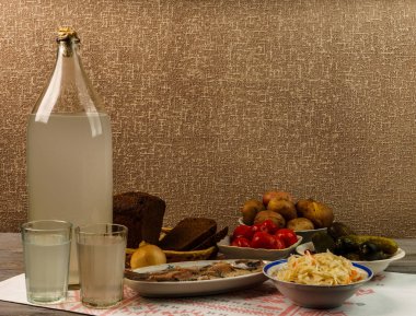 Ukrayna ulusal içecek ve atıştırmalık. Eski tahta masadaki büyük şişe ve bir bardak kaçak içki. Rus votka ve aperatif.