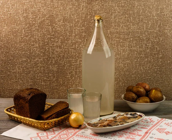 Ukrayna ulusal içecek ve atıştırmalık. Eski tahta masadaki büyük şişe ve bir bardak kaçak içki. Rus votka ve aperatif.