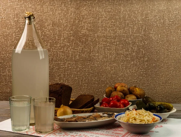 Ukrayna ulusal içecek ve atıştırmalık. Eski tahta masadaki büyük şişe ve bir bardak kaçak içki. Rus votka ve aperatif.