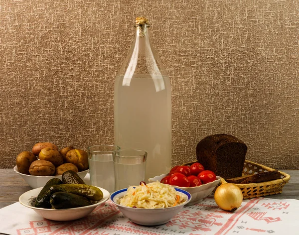 Ukrayna ulusal içecek ve atıştırmalık. Eski tahta masadaki büyük şişe ve bir bardak kaçak içki. Rus votka ve aperatif.