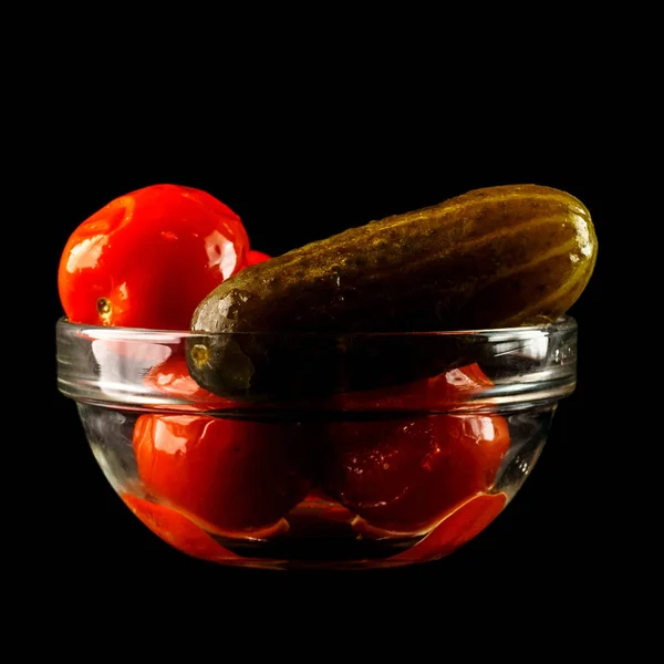 Соленый огурец с помидорами в стеклянной вазе. Чаша красных помидоров и огурцов, изолированных на черном фоне — стоковое фото