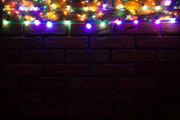 Corona y guirnaldas de bombillas de colores. Fondo navideño con luces y espacio libre de texto. Frontera de luces de Navidad. Luces de Navidad de colores brillantes sobre un fondo de pared de ladrillo. Año Nuevo . —  Fotos de Stock