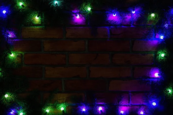 Krans en slingers van gekleurde gloeilampen. Kerstmis achtergrond met verlichting en vrije tekst ruimte. De grens van de lichten van Kerstmis. Gloeiende kleurrijke Kerstverlichting op een bakstenen muur achtergrond. Nieuwjaar. — Stockfoto