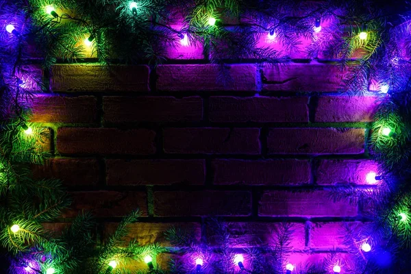 Věnce a girlandy barevné žárovky. Vánoční pozadí se světly a volné místo. Vánoční světla hranice. Zářící barevná vánoční světla na pozadí cihlovou zeď. Nový rok. — Stock fotografie