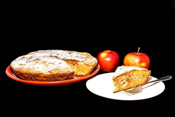 Manzanas frescas y un trozo de tarta de manzana espolvoreada con azúcar en polvo sobre el fondo negro . — Foto de Stock