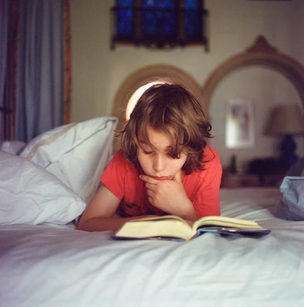 Αγόρι ξεκούραστη στο κρεβάτι, διαβάζοντας το βιβλίο — Φωτογραφία Αρχείου