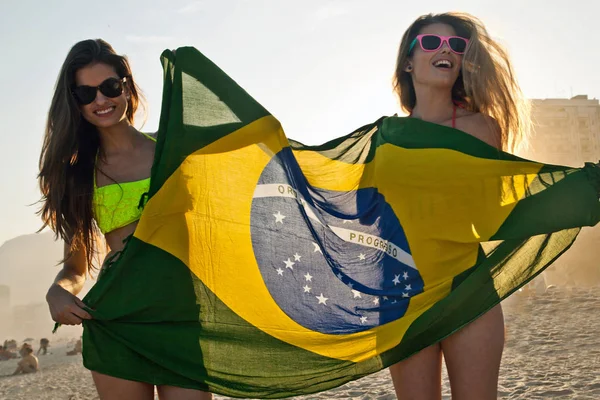 两个拿着巴西国旗在海滩玩乐的年轻女人 — 图库照片